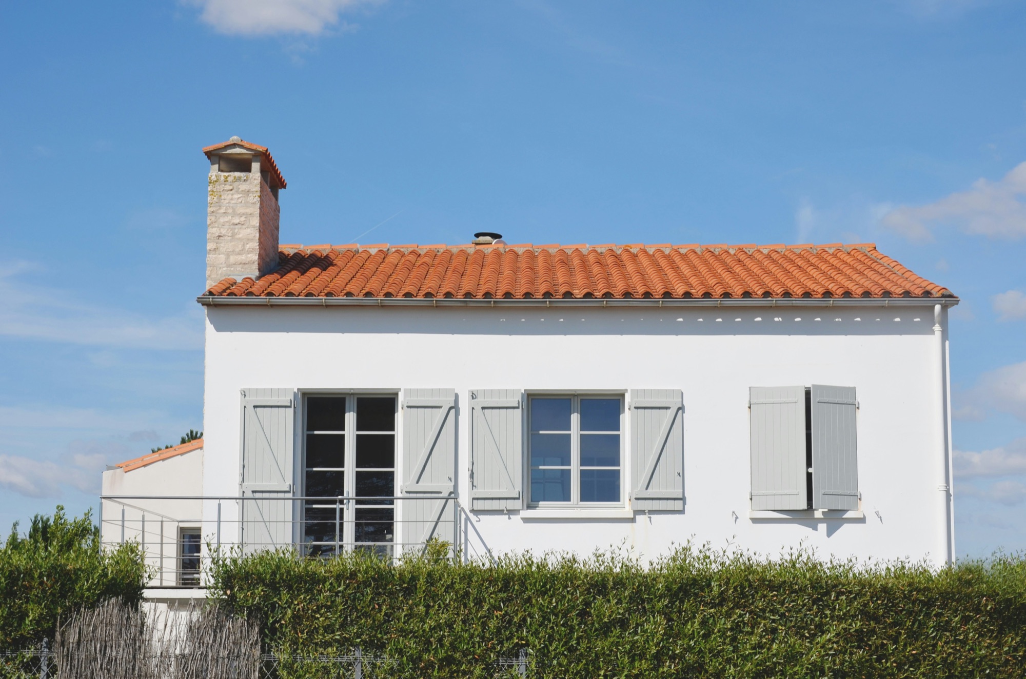 Maison blanche aux volets gris, avec un toit de tuiles et une cheminée