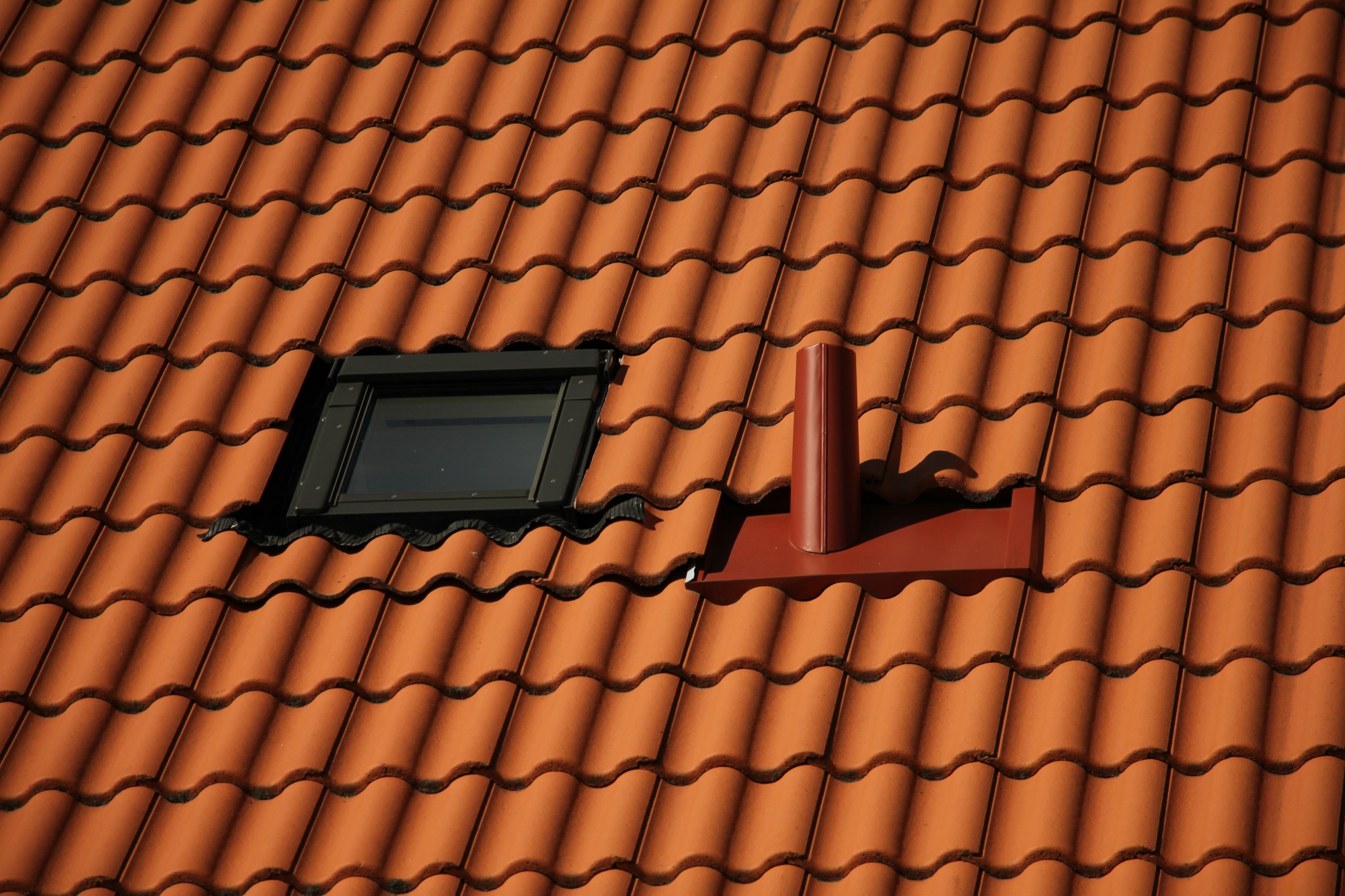 Fenêtre de toit posée dans une toiture en tuiles, à côté d’une sortie de ventilation