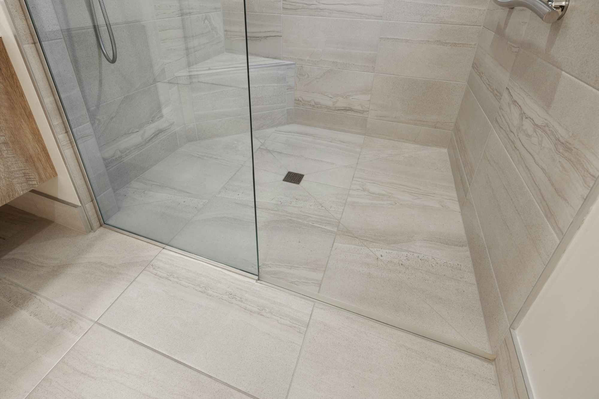 Douche à l’italienne carrelée de grands carreaux clairs, avec une paroi en verre et une bonde au sol